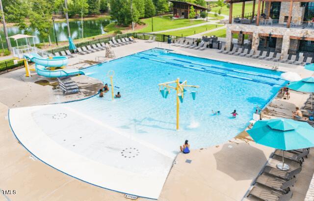 community pool with fence, a patio, a water slide, and a water play area