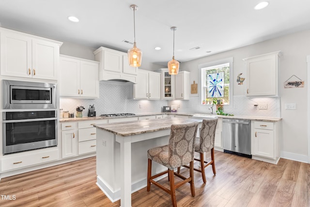 kitchen with stainless steel appliances, decorative backsplash, white cabinetry, and light wood-style floors
