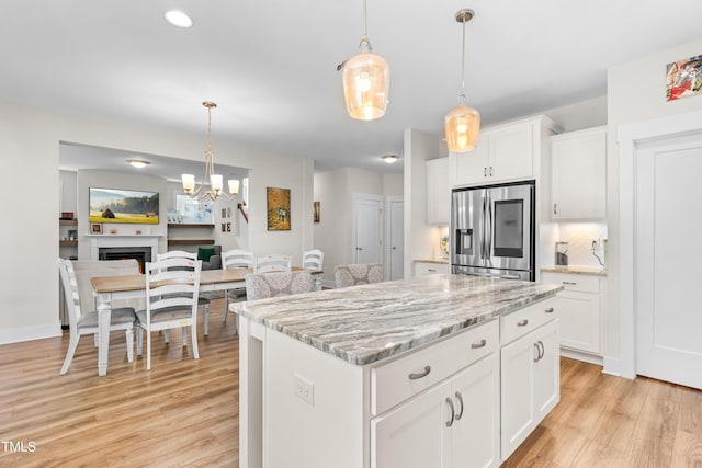 kitchen featuring stainless steel refrigerator with ice dispenser, a center island, hanging light fixtures, white cabinets, and light wood finished floors