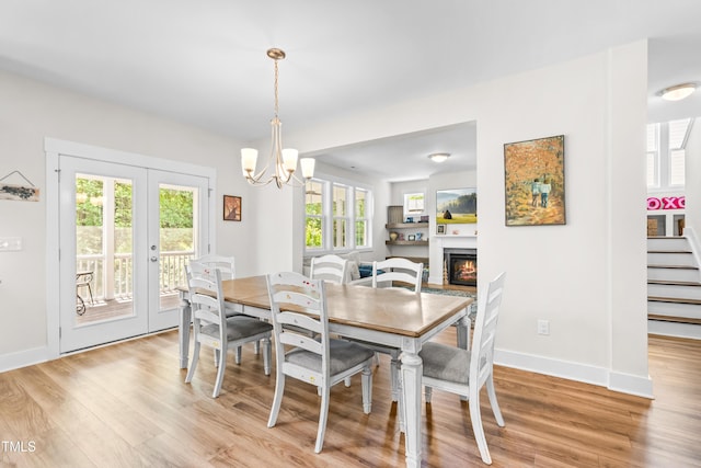 dining area with a chandelier, french doors, light wood-style flooring, baseboards, and a lit fireplace