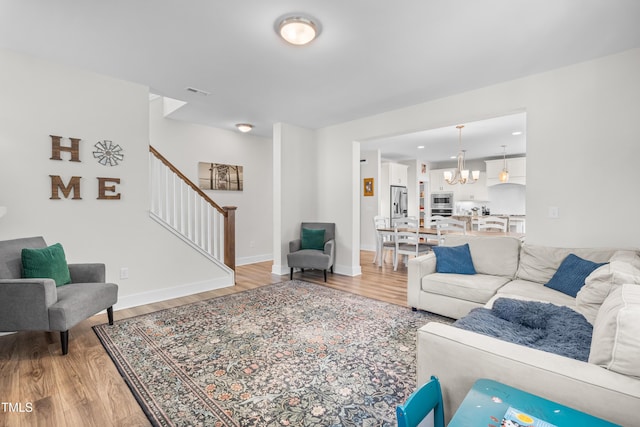 living room with visible vents, an inviting chandelier, stairs, light wood-style floors, and baseboards