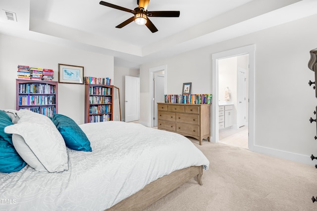 bedroom with connected bathroom, light carpet, a raised ceiling, baseboards, and visible vents