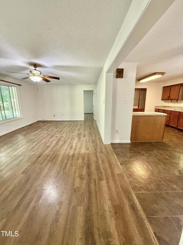 unfurnished living room with baseboards, dark wood-style flooring, a textured ceiling, and ceiling fan