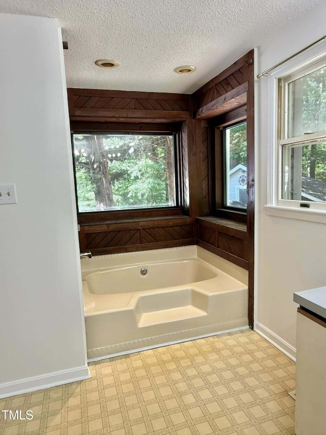full bath featuring a textured ceiling, tile patterned floors, baseboards, and a garden tub