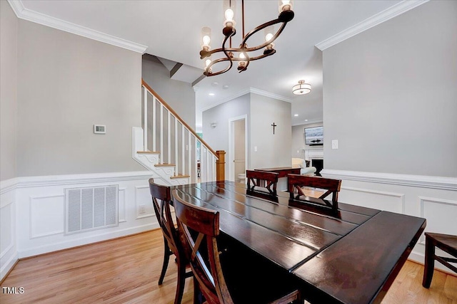 105 Wittenham Dr, Cary, NC 27519 - dining area with crown molding, a chandelier, a decorative wall, light wood-style floors, and a wainscoted wall