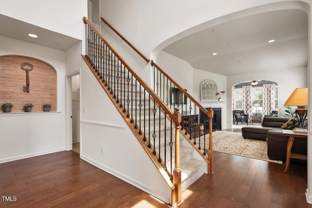stairway featuring wood-type flooring, arched walkways, recessed lighting, and a fireplace