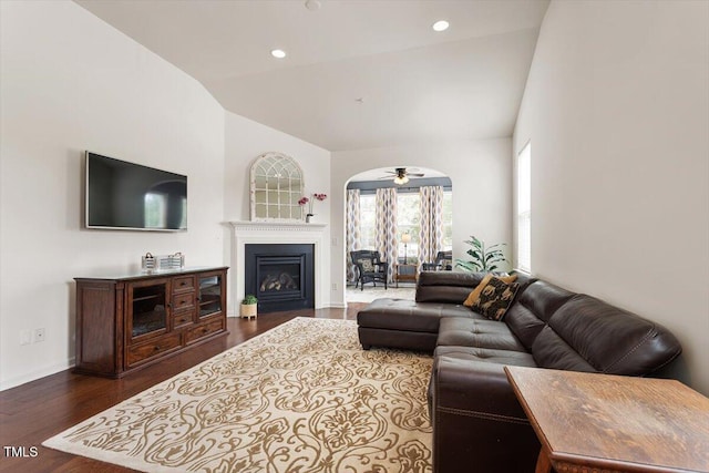 living room with ceiling fan, high vaulted ceiling, a glass covered fireplace, baseboards, and dark wood-style floors