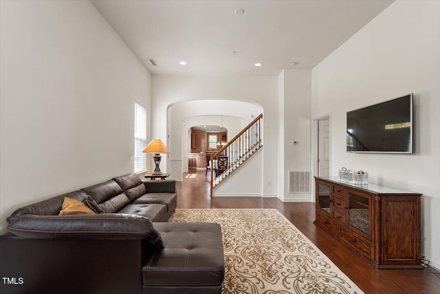 living room with visible vents, arched walkways, baseboards, dark wood-style floors, and stairs