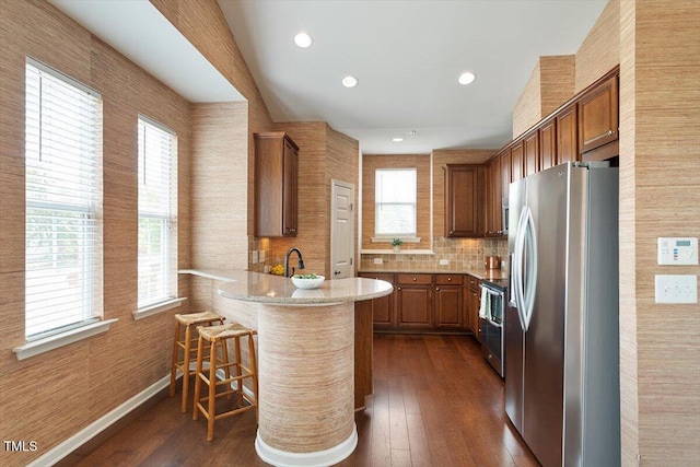 kitchen with a breakfast bar area, dark wood finished floors, a peninsula, stainless steel appliances, and recessed lighting