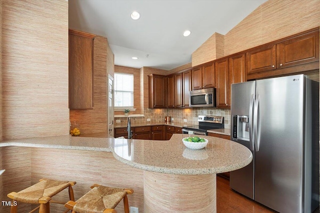 kitchen featuring decorative backsplash, a peninsula, light stone counters, vaulted ceiling, and stainless steel appliances