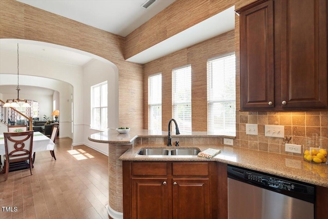 kitchen with arched walkways, stainless steel dishwasher, a sink, a peninsula, and a chandelier
