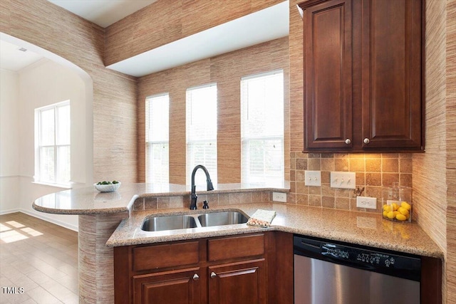kitchen with stainless steel dishwasher, a sink, light stone counters, and a healthy amount of sunlight