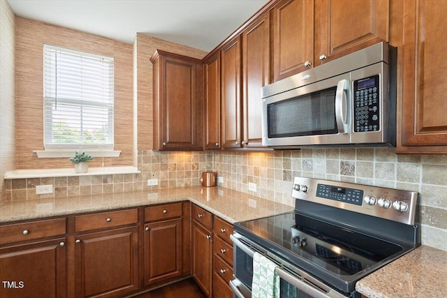 kitchen featuring light stone counters, brown cabinetry, backsplash, and stainless steel appliances