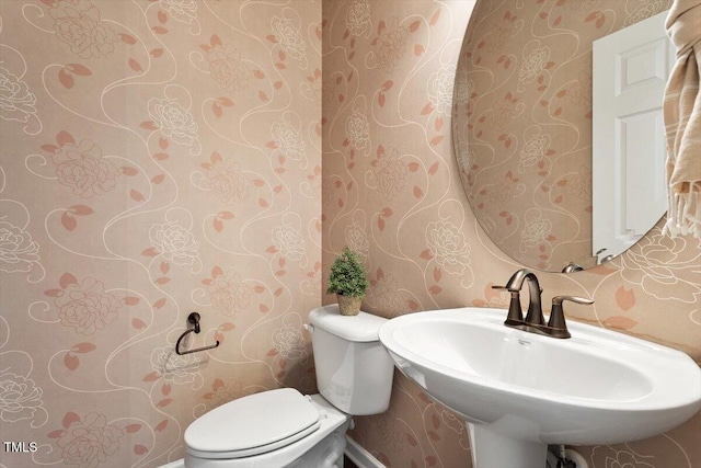 bathroom with toilet, wallpapered walls, and a sink