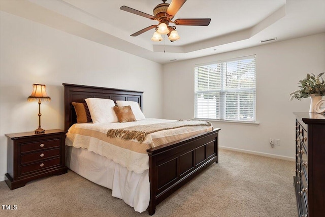 bedroom featuring ceiling fan, light colored carpet, a raised ceiling, baseboards, and visible vents