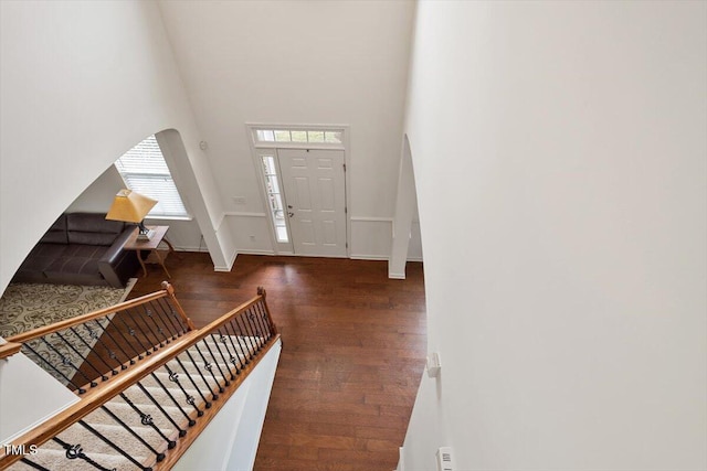 entrance foyer with a towering ceiling, arched walkways, wood finished floors, stairway, and baseboards