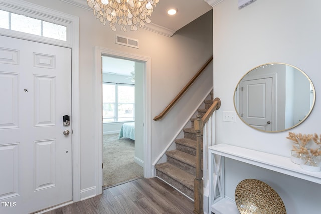 foyer entrance featuring visible vents, wood finished floors, baseboards, a notable chandelier, and stairs