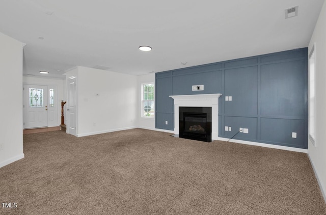 unfurnished living room featuring carpet floors, a fireplace with flush hearth, and a healthy amount of sunlight