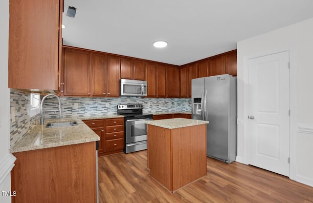 kitchen with a sink, appliances with stainless steel finishes, light stone counters, and wood finished floors
