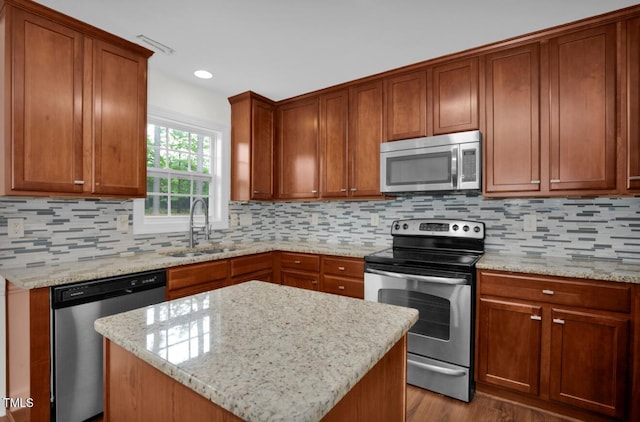 kitchen featuring decorative backsplash, wood finished floors, a sink, light stone counters, and stainless steel appliances