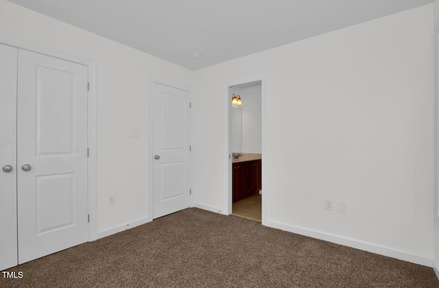 unfurnished bedroom with dark colored carpet, baseboards, and ensuite bath
