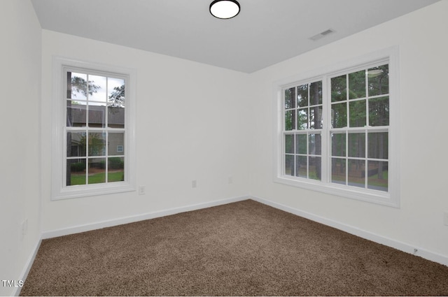 spare room featuring baseboards, visible vents, and dark carpet