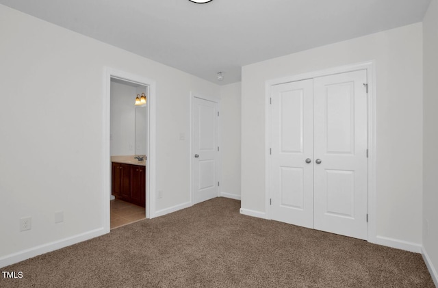 unfurnished bedroom with a closet, carpet flooring, baseboards, and ensuite bathroom