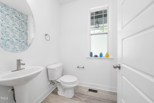 half bathroom with visible vents, wood finished floors, a sink, baseboards, and toilet