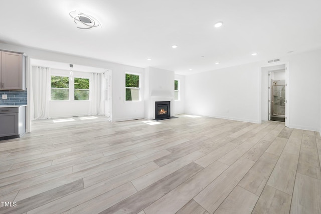 unfurnished living room featuring visible vents, baseboards, recessed lighting, a fireplace with flush hearth, and light wood finished floors