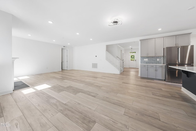 unfurnished living room featuring visible vents, stairs, baseboards, recessed lighting, and light wood-style flooring