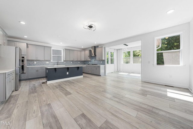 kitchen with freestanding refrigerator, a breakfast bar, wall chimney range hood, light countertops, and gray cabinetry