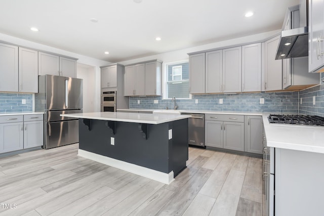 kitchen with appliances with stainless steel finishes, a breakfast bar area, gray cabinets, tasteful backsplash, and a kitchen island