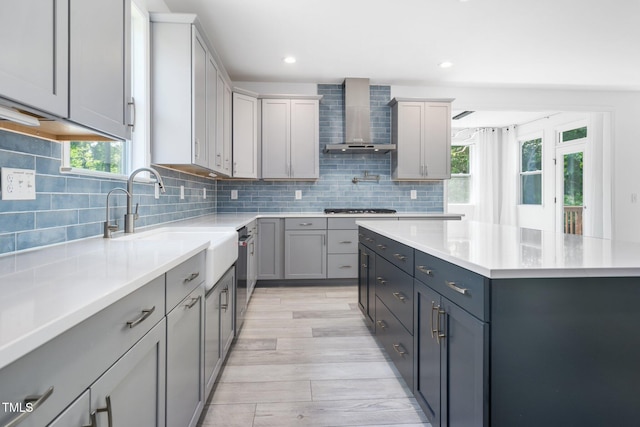 kitchen with light countertops, wall chimney exhaust hood, gas stovetop, backsplash, and gray cabinetry