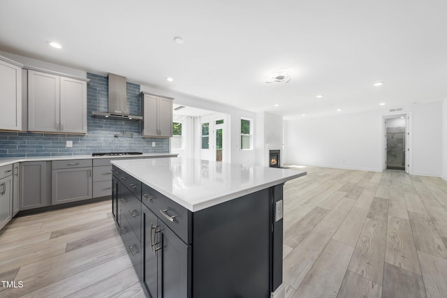 kitchen with light wood finished floors, light countertops, gray cabinets, wall chimney exhaust hood, and a center island