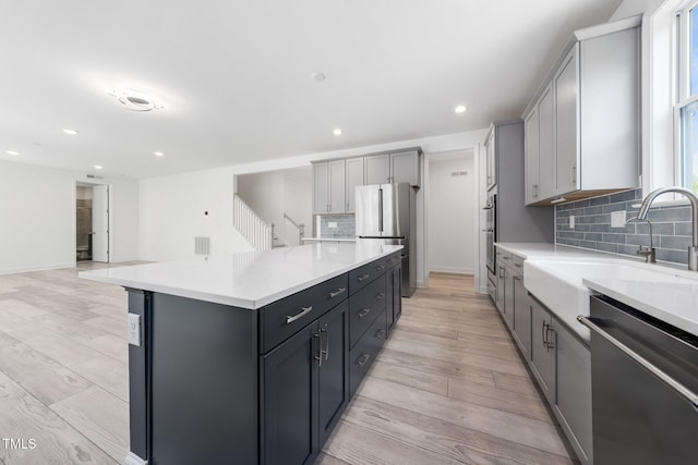 kitchen featuring light wood-style floors, decorative backsplash, stainless steel appliances, and a sink