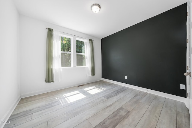 unfurnished room featuring baseboards, light wood-style flooring, and visible vents