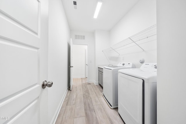 laundry room featuring washing machine and clothes dryer, light wood-style flooring, cabinet space, and visible vents