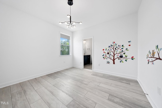 empty room featuring baseboards, an inviting chandelier, and light wood finished floors