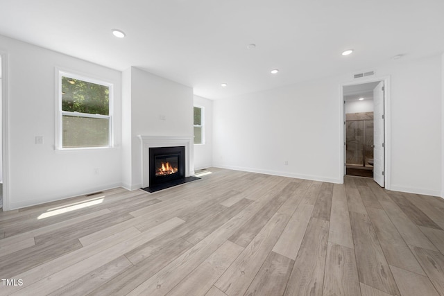 unfurnished living room featuring recessed lighting, visible vents, a glass covered fireplace, and light wood-style flooring