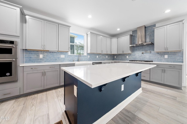 kitchen featuring wall chimney range hood, gray cabinets, stainless steel appliances, and a sink