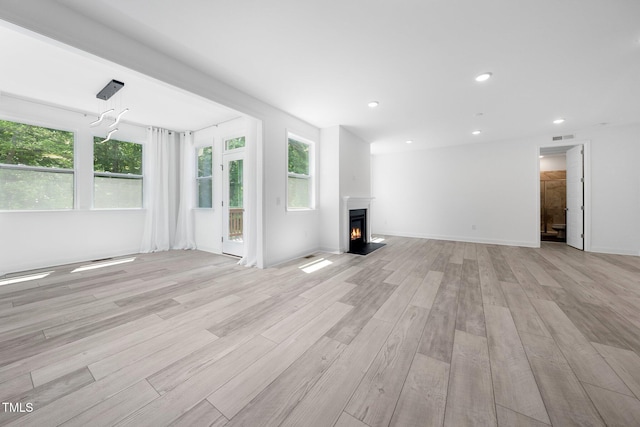 unfurnished living room with recessed lighting, light wood-style flooring, a warm lit fireplace, and visible vents