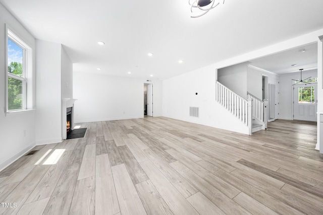 unfurnished living room with stairway, a warm lit fireplace, light wood-type flooring, and visible vents