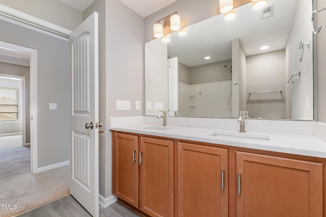 full bathroom with double vanity, a tile shower, a sink, and wood finished floors