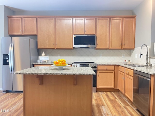 kitchen with a sink, light wood-style flooring, light stone counters, and appliances with stainless steel finishes