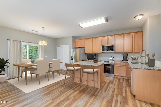 kitchen with light wood-style floors, appliances with stainless steel finishes, decorative backsplash, and a sink