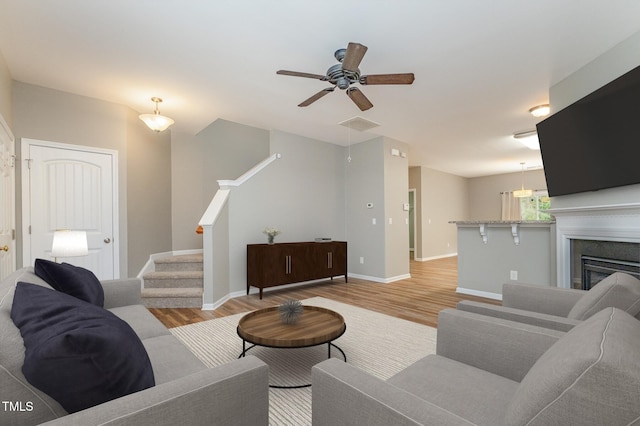 living room with light wood-style flooring, a fireplace, stairway, baseboards, and ceiling fan