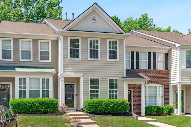 townhome / multi-family property with roof with shingles and brick siding