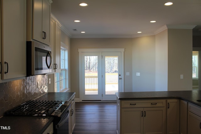 kitchen featuring dark countertops, range with gas stovetop, stainless steel microwave, a wealth of natural light, and dark wood-type flooring