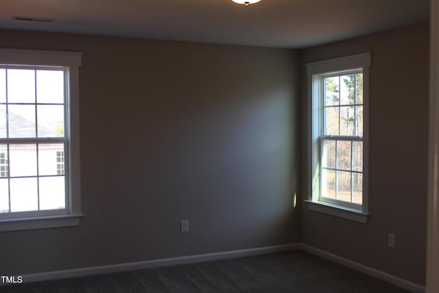 spare room featuring baseboards, visible vents, and dark colored carpet