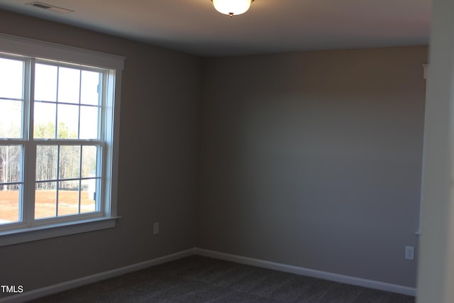 unfurnished room featuring dark carpet, baseboards, a wealth of natural light, and visible vents